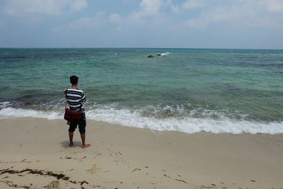 Rear view of man standing on beach against sky