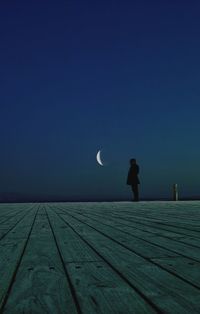 Man standing on pier against blue sky at night