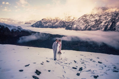 Woman standing on snowcapped mountain against sky