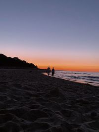 Silhouette people on beach against clear sky during sunset