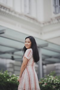 Portrait of smiling young woman standing against built structure