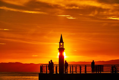 Scenic view of sea with silhouette people and lighthouse against sky during sunset