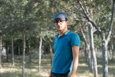 Mature man wearing cap and eyeglasses standing against trees in forest