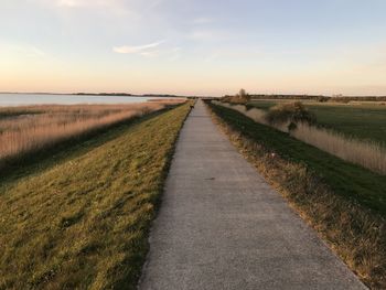 Empty road amidst field against sky during sunset