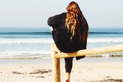 Rear view of woman standing on beach against clear sky