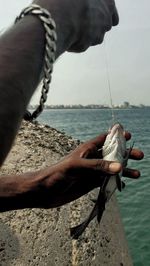 Close-up of hand holding rope against sea