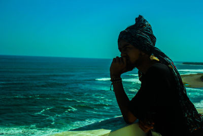 Side view of man sitting on beach against clear sky