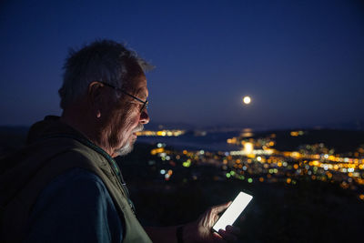 Side view of man using smart phone against sky at night