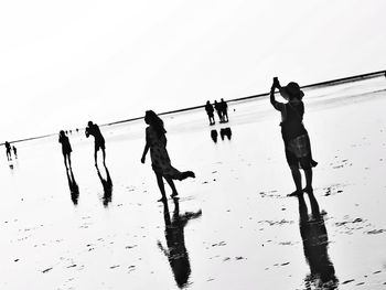 Silhouette people on beach against clear sky