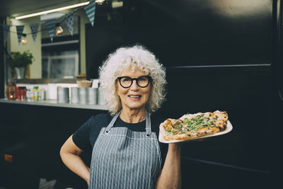 Portrait of senior owner with street food against commercial land vehicle in city