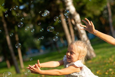 Girl and boy hands catching bubbles against trees