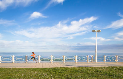 Woman running on promenade against sky