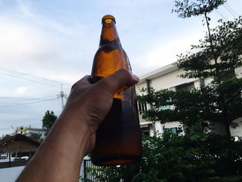 Low section of person holding bottle against sky