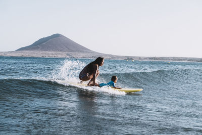 Pulled back view of mother and son surfing a small wave at sea