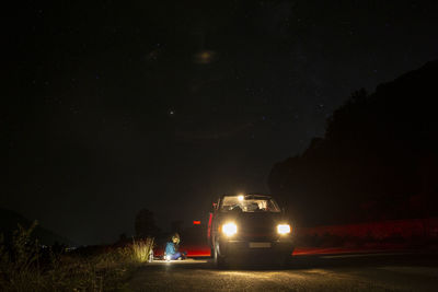 Female camper sitting in front of mini van in middle of rural road at night