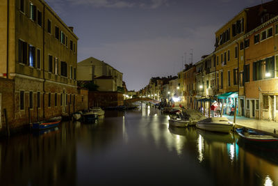 Boats moored in canal amidst buildings in city at night