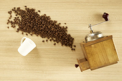 High angle view of coffee beans with grinder on wooden table