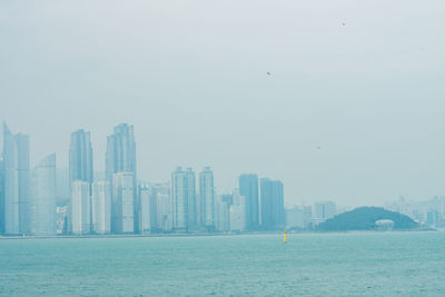 Urban skyline by sea against sky