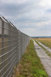 Empty road amidst field against sky
