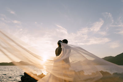 Woman with umbrella against sky during sunset