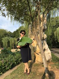 Portrait of woman holding leaf while standing by tree