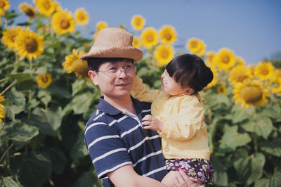 Man holding daughter against sunflowers