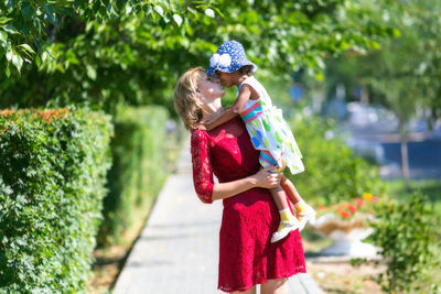 Mother carrying daughter at park on sunny day