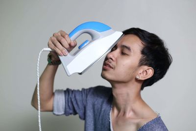 Young man holding iron against white background