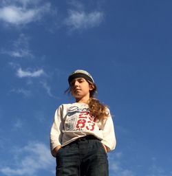 Low angle portrait of girl standing with hands in pockets against sky