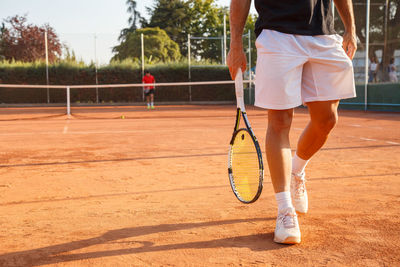 Low section of young man walking with racket at tennis court