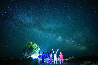 People standing on tree against star field at night