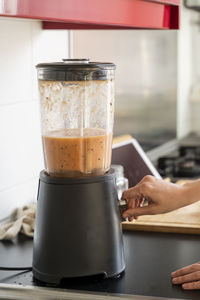 Young woman making smoothie through blender in kitchen at home