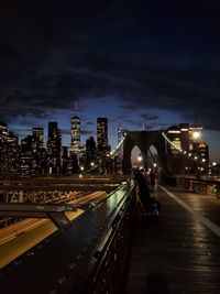 Illuminated street amidst buildings against sky at night