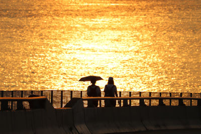 Silhouette people on railing against sea during sunset