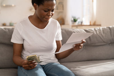 Woman holding money and bill sitting at home