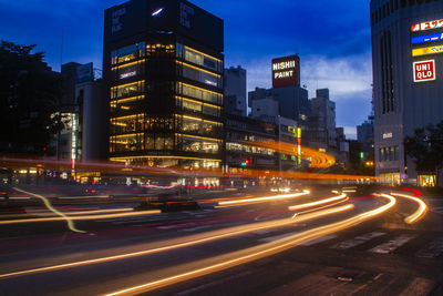 Light trails on road by illuminated buildings in city at night