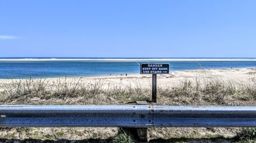 Information sign by sea against clear blue sky