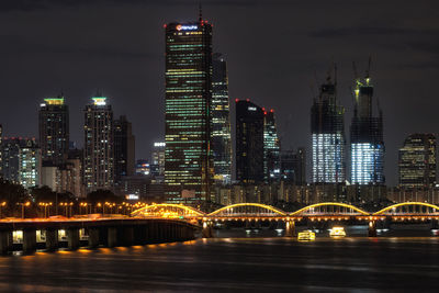 Illuminated bridge by buildings against sky at night