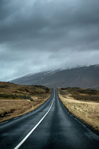 Empty road along landscape against cloudy sky