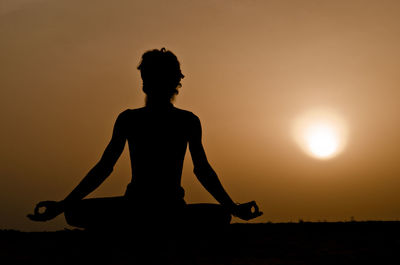 Silhouette man with arms raised against sky during sunset