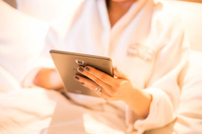 Midsection of woman using mobile phone on bed