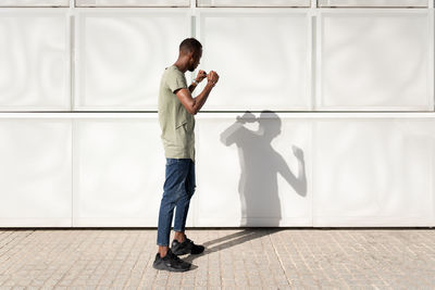 Side view of african american male standing in city in fighting position and battling with shadow on sunny day