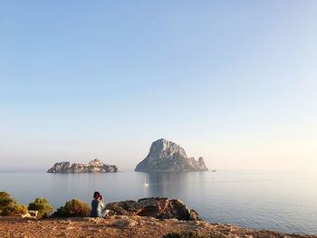 Man standing on cliff by sea against clear sky