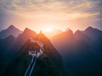 Man standing on steps in mountain against sky during sunset