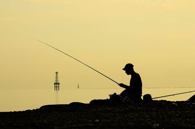 Silhouette man fishing at sunset