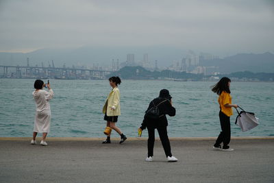 Rear view of people at beach against sky in city