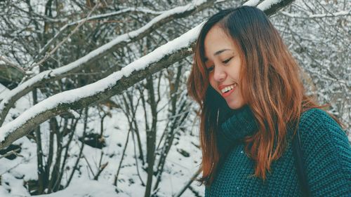 Close-up of smiling young woman against bare trees in forest during winter