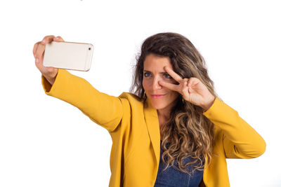 Portrait of woman photographing with mobile phone against white background