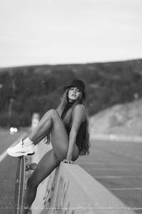 Portrait of young woman sitting with skateboard outdoors