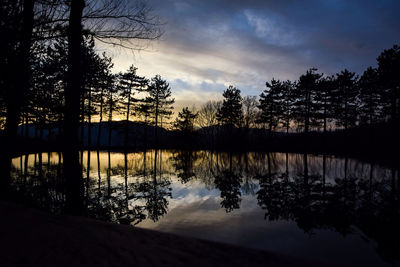 Silhouette trees by lake against sky during sunset